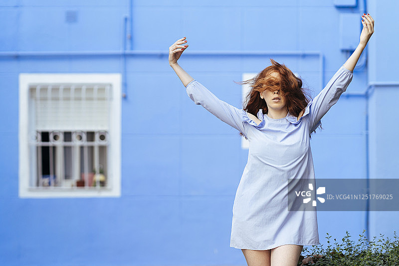 红发女人在蓝房子前举起双手图片素材