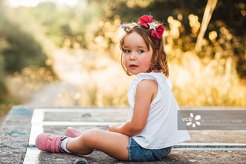 日落时分，小女孩坐在田野里的水泥平台上图片素材