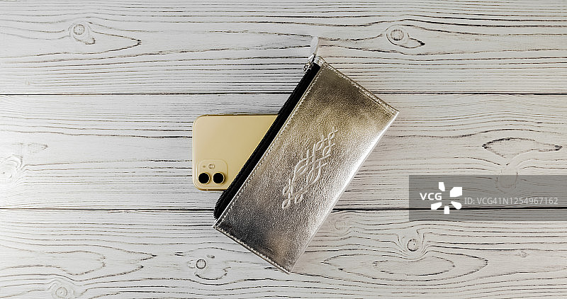黑色扣带的银色钱包，木质背景上有两个摄像头的昂贵智能手机。前视图。Flatlay图片素材