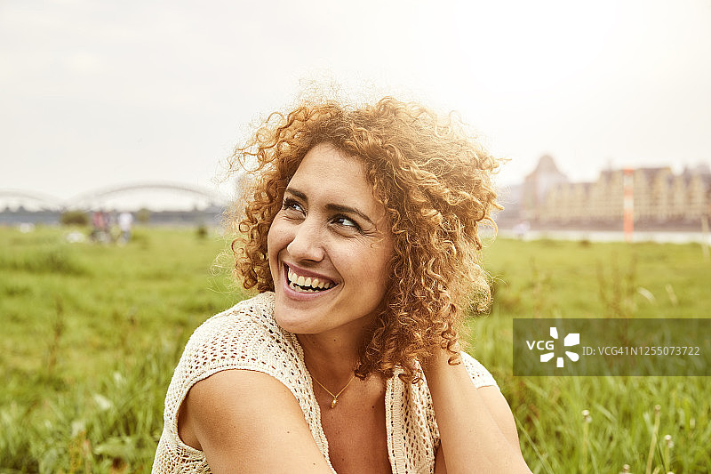 微笑的女人坐在草地上，向旁边看的肖像图片素材