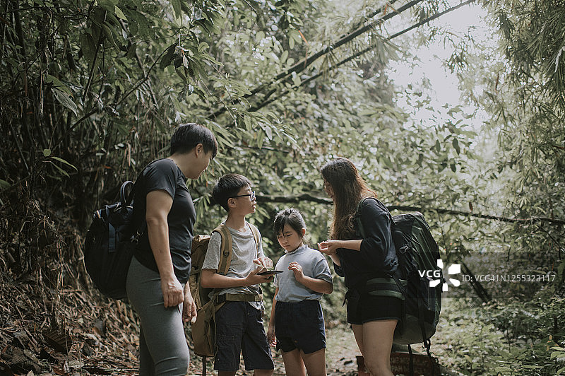 一个有两个孩子的亚洲华人家庭早上站在热带雨林前，用智能手机导航查看地图图片素材