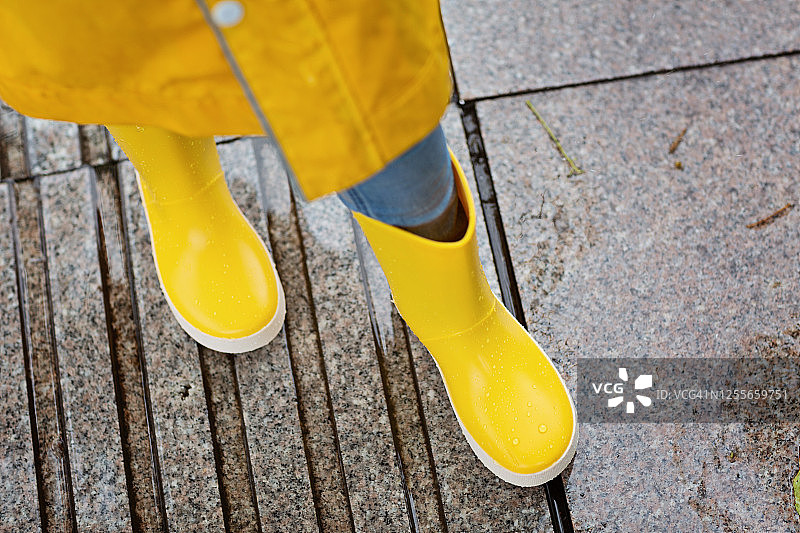 可爱的小女孩穿着黄色雨衣和胶靴在雨中户外散步。天气恶劣，夏季热带风暴，秋季时尚概念图片素材