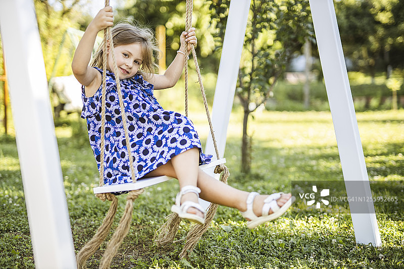 一个快乐的小女孩坐在秋千上，面带微笑图片素材