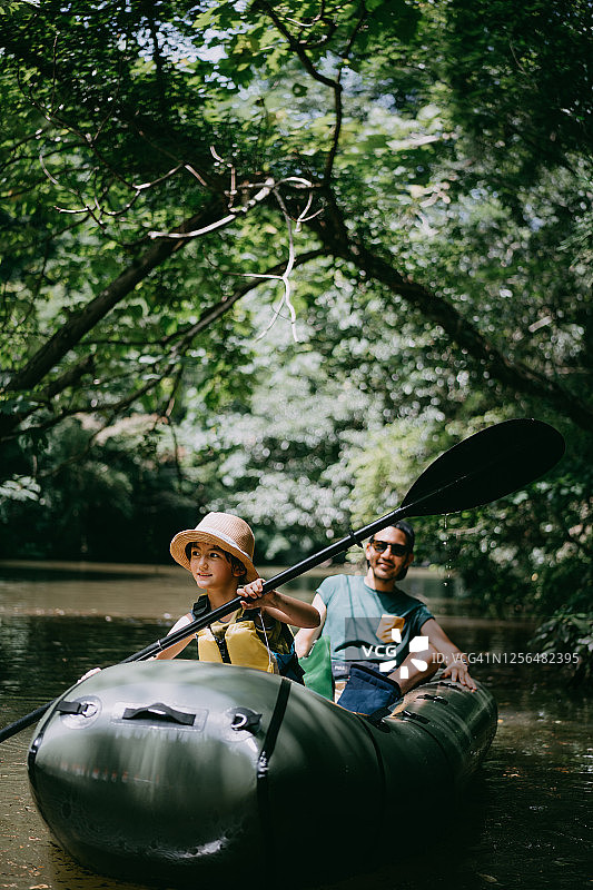 小女孩和父亲划着小舟穿过森林里的河流图片素材