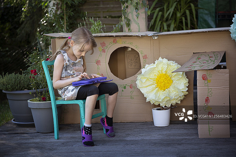 孩子使用数字平板电脑和坐在椅子上，在一个自制的院子里的藏身之处由回收纸板图片素材
