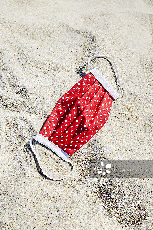 高角度的观点，一个红色的自制面膜在海滩上，度假与一个保护性的面膜图片素材