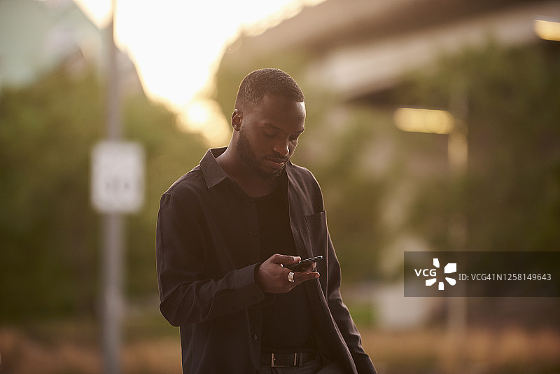 一个年轻人在城市街道上发短信。图片素材