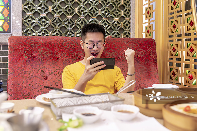 亚洲男人在晚餐后玩手机游戏图片素材