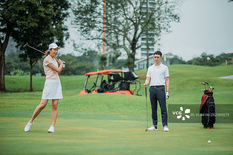 亚洲华裔年轻女高尔夫球手在高尔夫球场上把球敲向高尔夫球洞图片素材