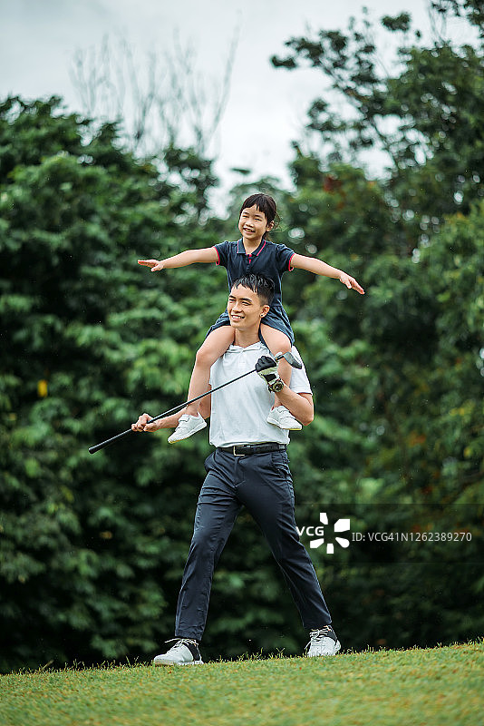 亚洲华人微笑年轻男子高尔夫球与他的女儿在高尔夫球场上图片素材