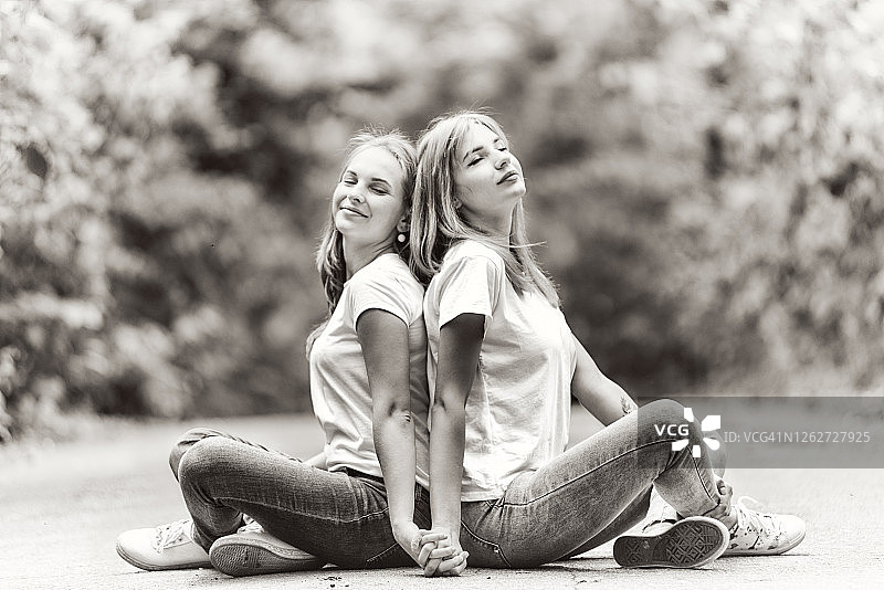 两个年轻女人背靠背坐在公园的路上图片素材