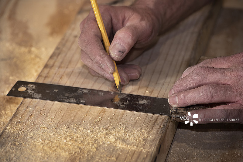 在建筑工地上，一名男木匠在木板上画了一条线，以便切割图片素材