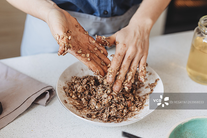 自制燕麦卷:妇女将燕麦卷与蜂蜜，椰子油和香料混合图片素材