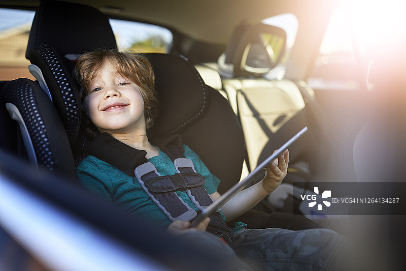 微笑的男孩坐在汽车后座上使用数码平板电脑的照片图片素材