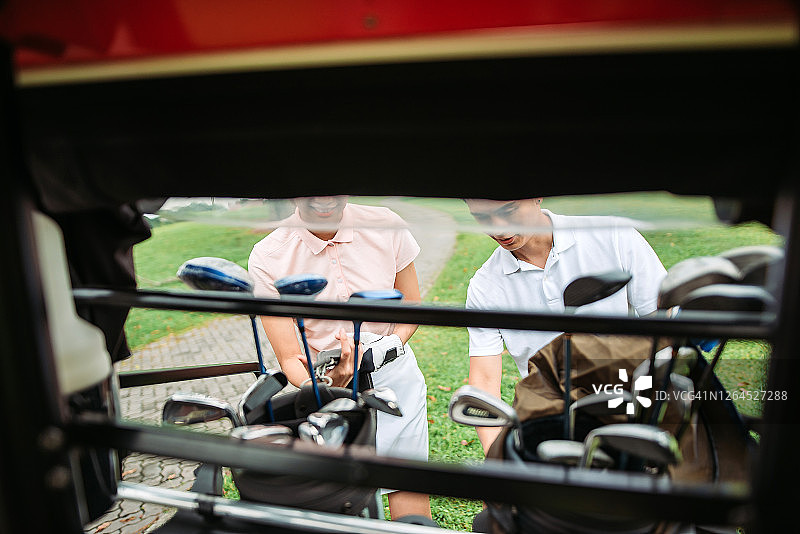 亚洲华人微笑年轻夫妇高尔夫球准备和从后面的高尔夫球车在绿色球场高尔夫球袋图片素材