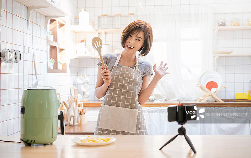 肖像美容博主亚洲女人评论烹饪油炸土豆食物与风扇跟随频道，录制视频飞行智能设备在家。网红女孩对社交媒体营销直播蒸的概念图片素材