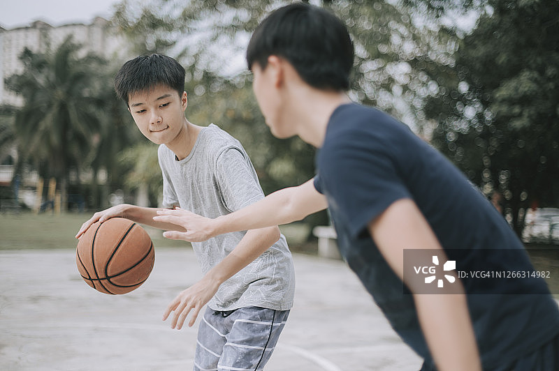 两个亚裔中国少年放学后在篮球场打篮球练习图片素材