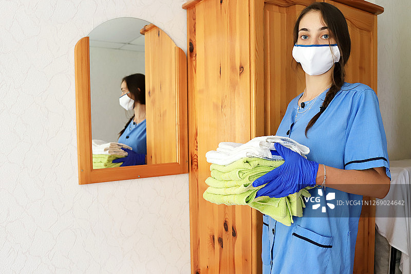 一个年轻的女佣在流行病期间打扫酒店房间图片素材