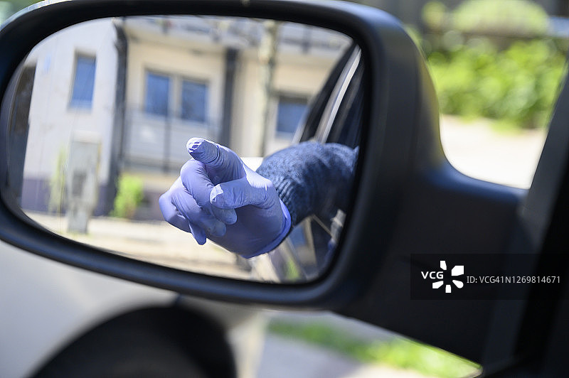 从汽车后视镜中看到有保护罩的人的手用食指指着什么东西。德国柏林。图片素材