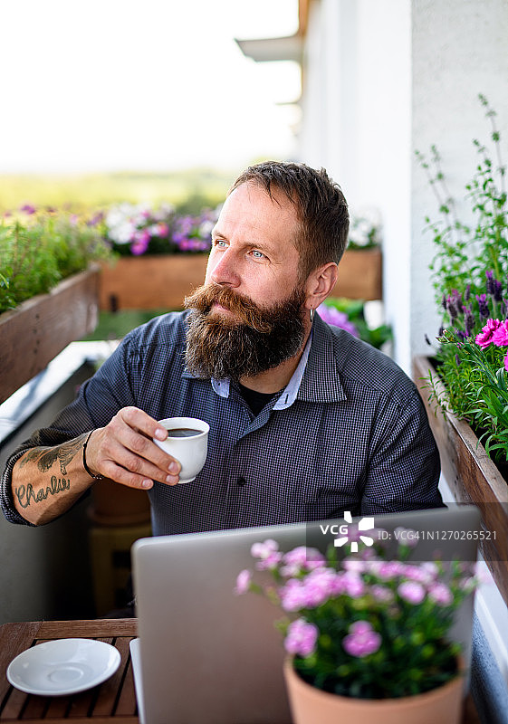 成熟的男人用咖啡和笔记本电脑在阳台上工作，家庭办公的概念。图片素材