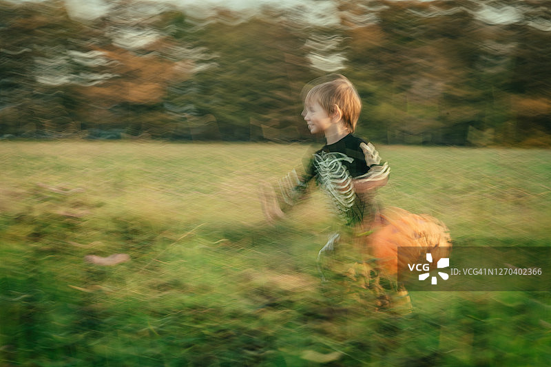 穿着骷髅装的男孩在万圣节的秋天挎着南瓜篮在户外奔跑图片素材