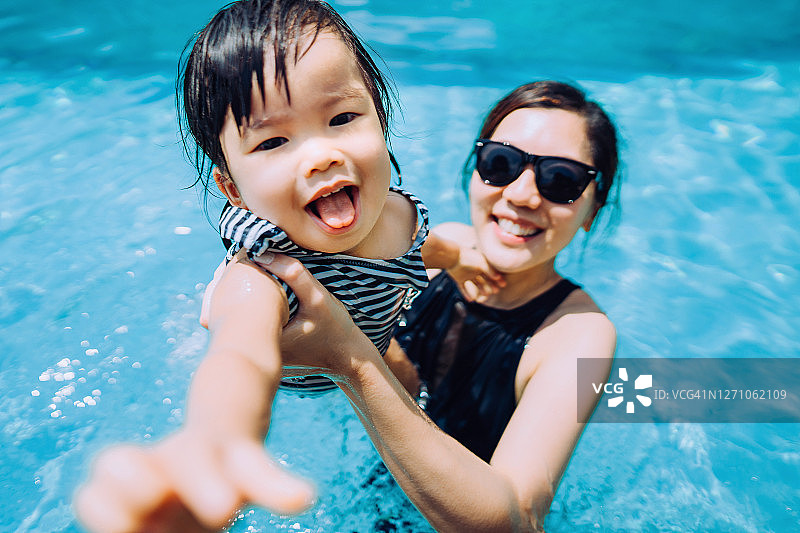 快乐的亚洲蹒跚学步的女孩愉快地微笑，享受家庭团聚的时间与母亲有乐趣的游泳池在夏天图片素材