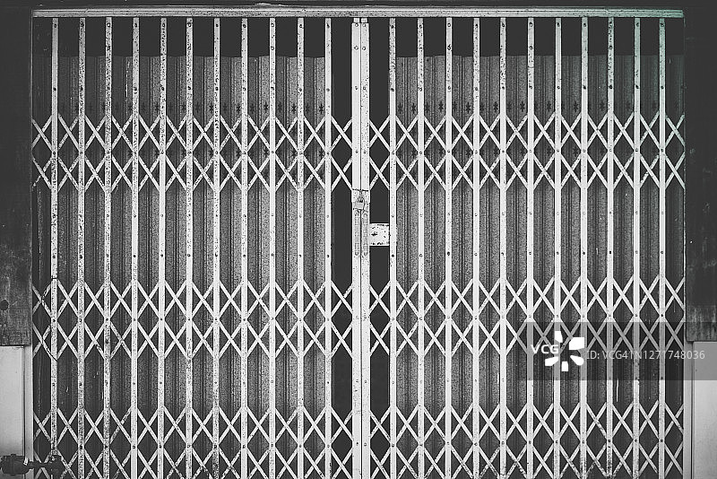 古老的钢制门。商店或工业建筑物上的百叶窗。陈旧生锈的金属卷帘门图案背景和纹理-复古风格-黑白滤镜处理。图片素材