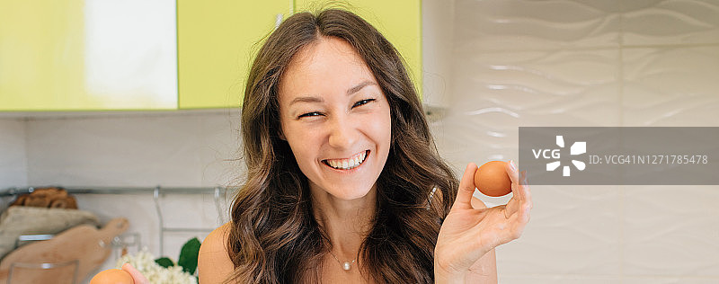 快乐的女人拿着两个鸡蛋站在厨房里图片素材