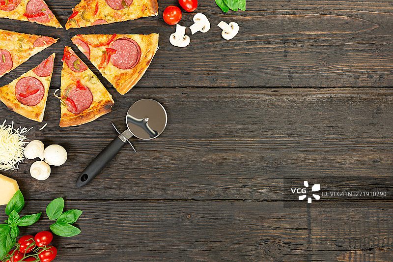 美味的热披萨配料和切披萨刀在黑色纹理的背景。俯视图图片素材