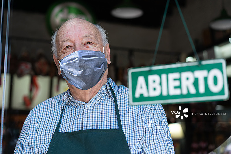 一家熟食店的高级店主，在疫情封锁后戴着防护口罩开始营业图片素材