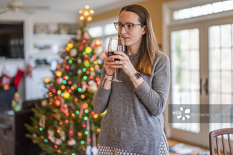 年轻女子在装饰好的圣诞树前喝红酒图片素材