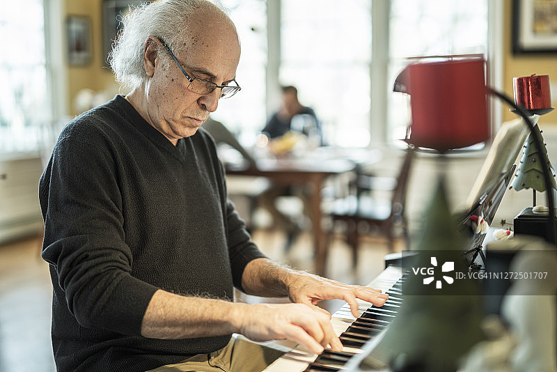 这位72岁的银发老人是一名音乐家，他正在为家人弹奏钢琴，而家人则在明亮宽敞的客厅里享用圣诞大餐。图片素材