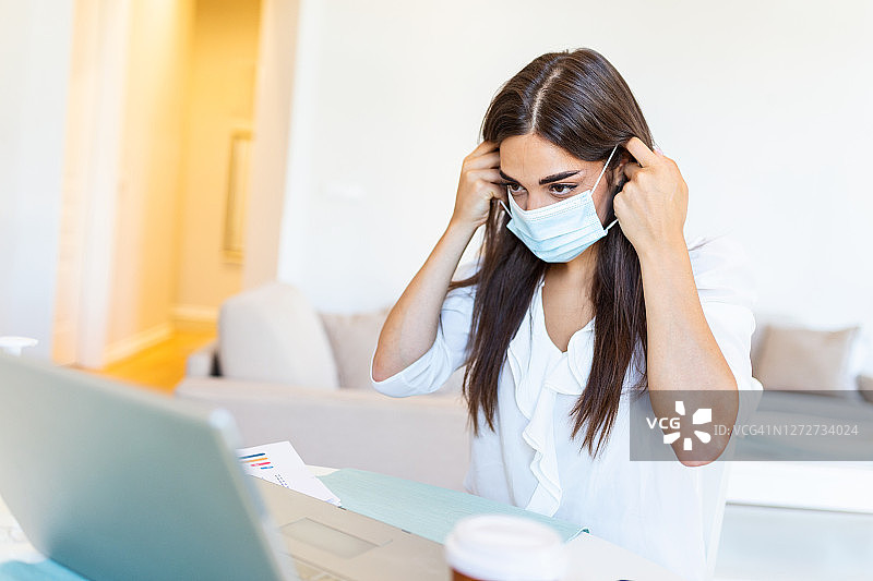 戴着防护面具在办公室用笔记本电脑工作的女商人。专注于千禧一代女员工经理戴着防护口罩在工作场所使用笔记本电脑，保持对冠状病毒危险的隔离措施。图片素材