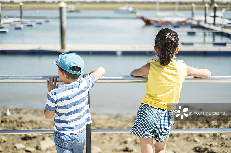 小孩子们靠在人行道的栏杆上观看港口里的船只图片素材