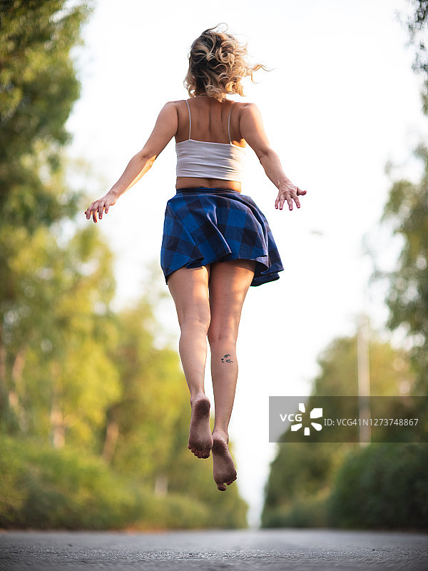 美丽的年轻女子跳上柏油路后视镜图片素材
