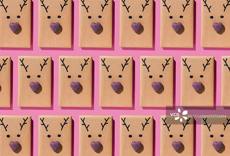 圣诞礼物用可爱的驯鹿脸包裹在粉红色的背景上，排成一排图片素材