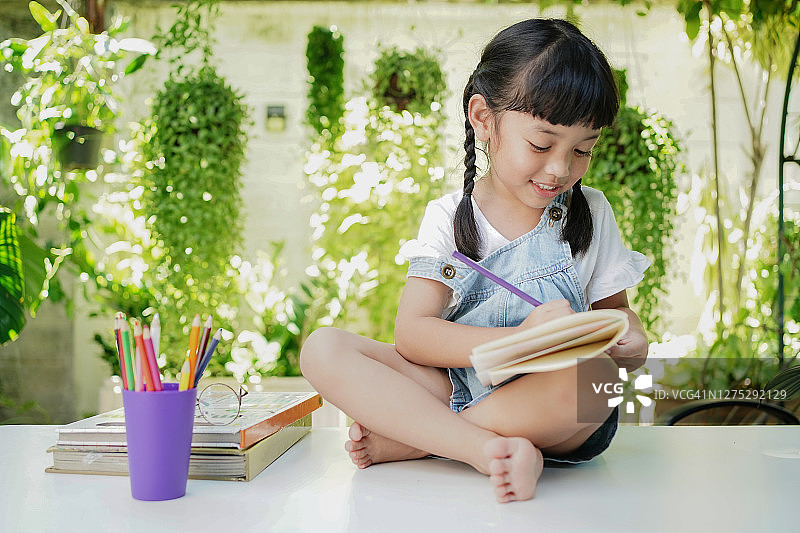 亚洲学生女孩在家里的作业书上画画和写字图片素材