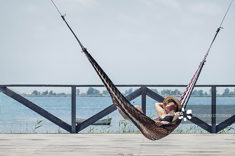 轻松的女人躺在吊床上的木板路在海上对晴朗的天空图片素材