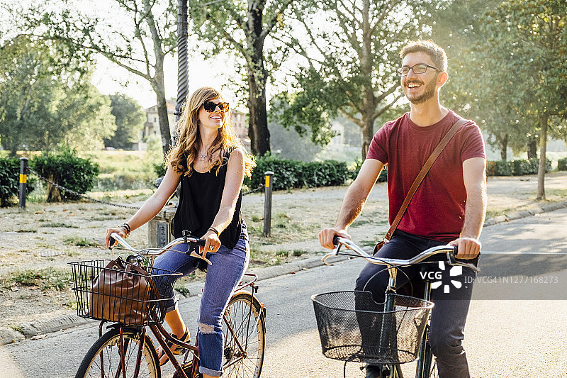 周末，幸福的情侣在公园的道路上骑自行车图片素材