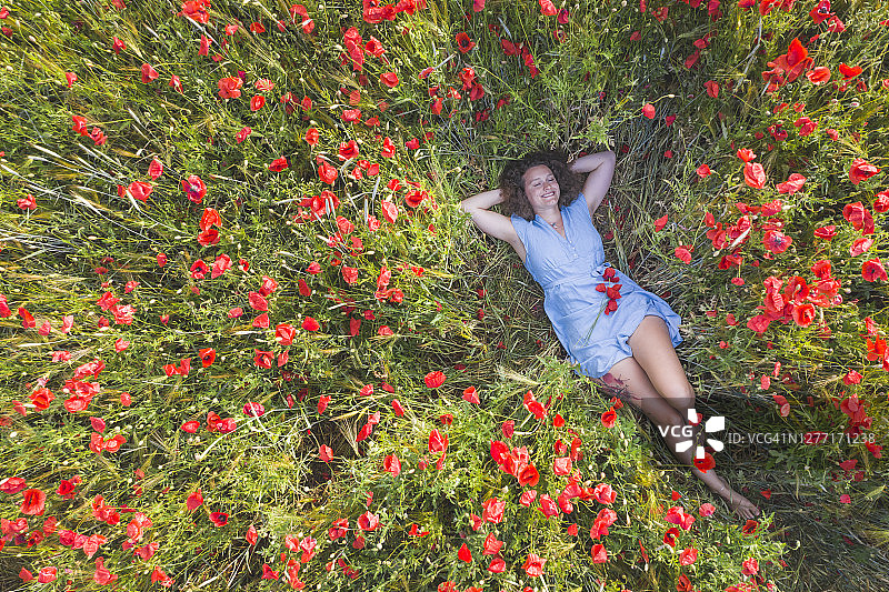 微笑的女人躺在罂粟田里，双手抱头图片素材