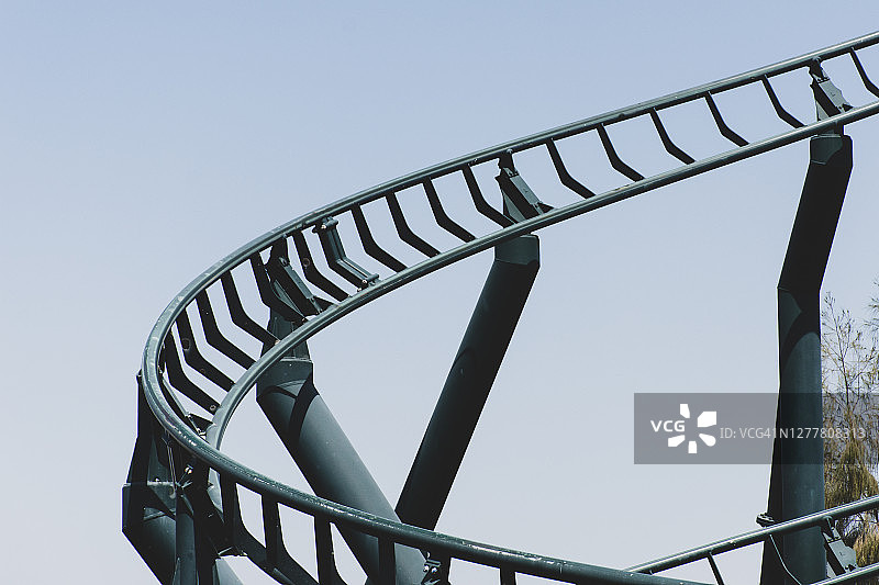 弧形过山车在一个主题或游乐园空绿色金属轨道和蓝天背景。图片素材