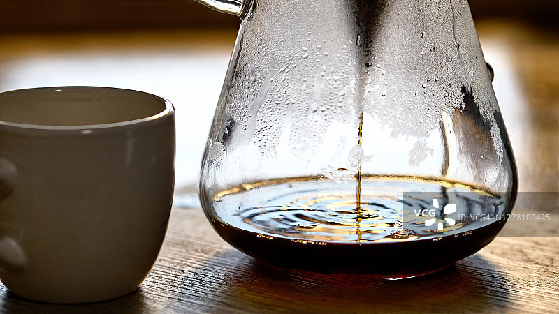 新煮的咖啡从倒滤器和磨碎的咖啡进入玻璃容器冷凝。图片素材