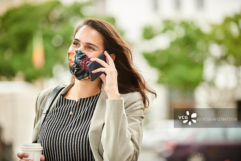 一个戴着保护面罩的女人在城市里走路时打电话图片素材