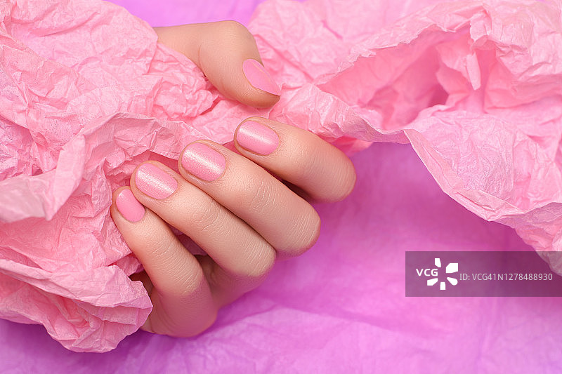 女性手与粉红色指甲设计。粉红色指甲油修剪过的手。女人的手拿着粉红色背景上的皱巴巴的纸。图片素材