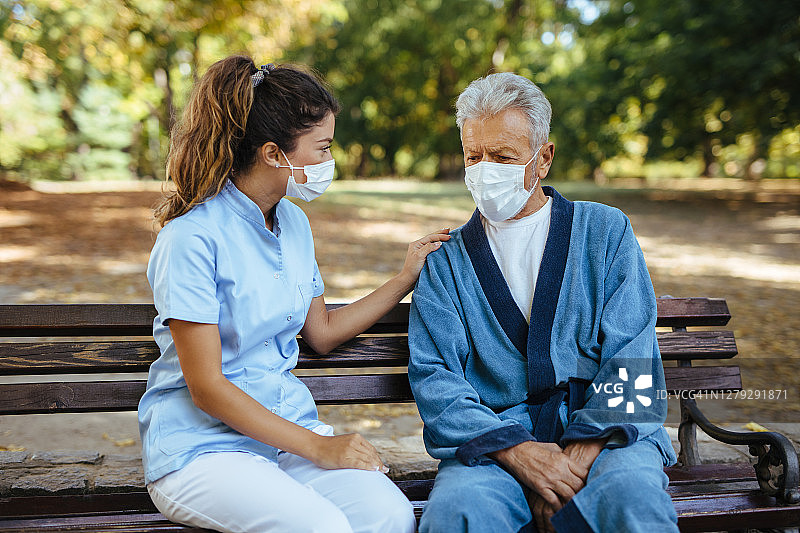 医护人员和戴防护口罩的老年人坐在长凳上交流图片素材