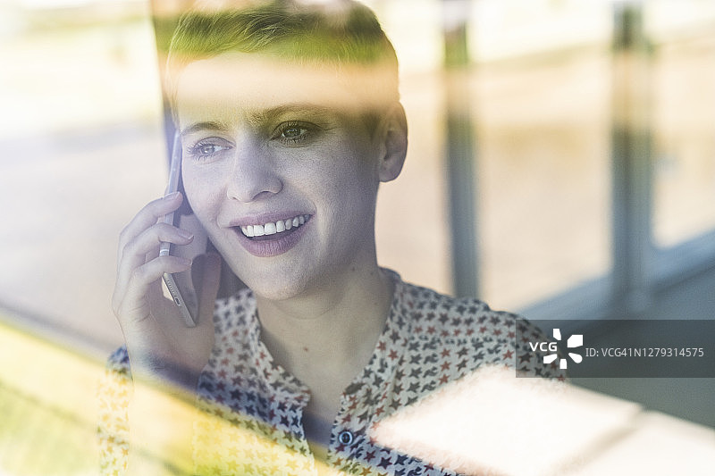 通过窗户看到的女企业家在办公室里通过手机聊天的特写图片素材