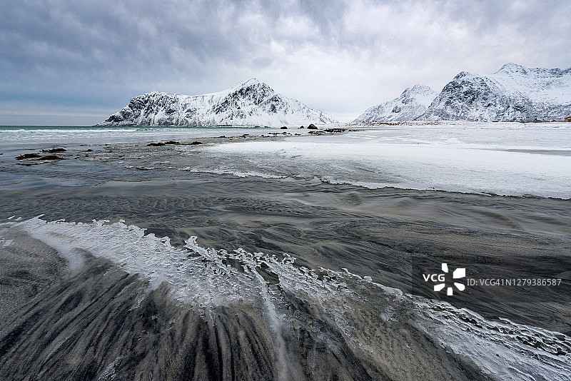 被罗浮敦群岛白雪覆盖的高峰所包围的冰冻海滩上的小溪图片素材