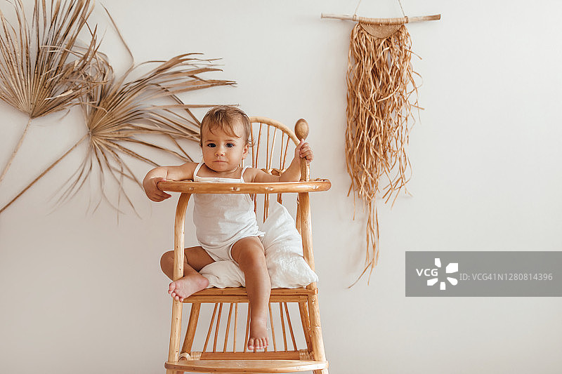 可爱的小女孩坐在生态木制儿童餐椅上。天然有机材料的婴儿房。“零浪费”的概念。图片素材