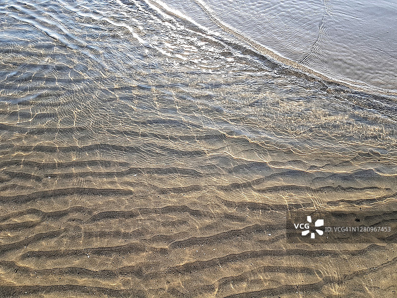 背景起伏的沙子和柔和的海浪到达海岸，与阳光反射图片素材