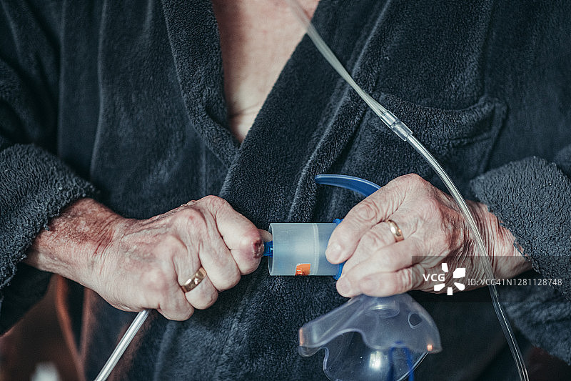 一位老人的手，他正在组装他的喷雾器治疗的部分，这有助于他更好地呼吸。图片素材
